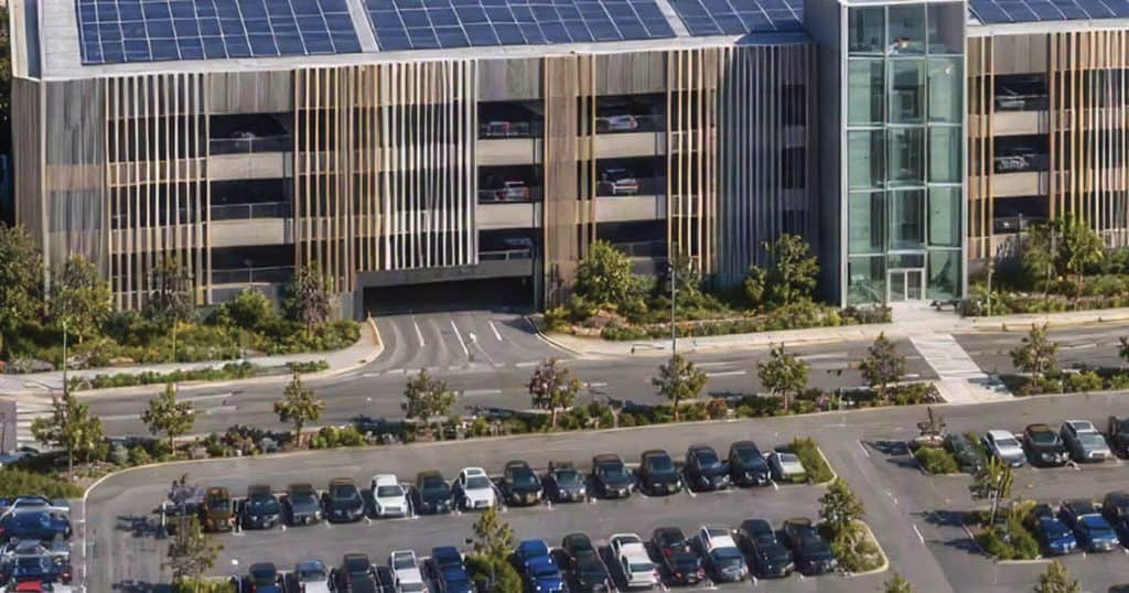 Modern multi-level parking garage with surrounding greenery and parking lot.