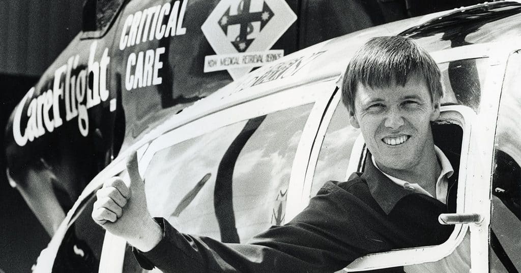 Young man smiling and giving a thumbs-up next to a helicopter.