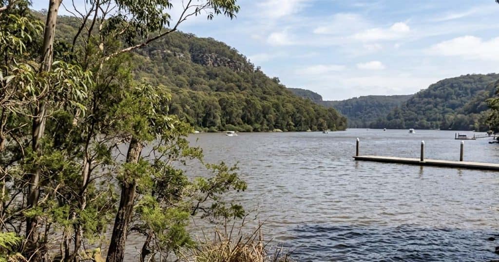 Scenic view of the Hawkesbury River with lush green hills and a clear sky.