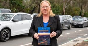 Woman holding a report titled 'Fairer Future' outdoors with parked cars behind.